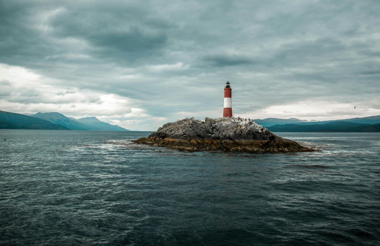 "Solitary lighthouse standing on a rocky island under a dramatic cloudy sky.